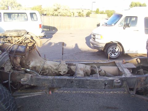 1978 Ford Bronco - The bare frame of a vehicle, showing its engine and transmission, sits between two vans.