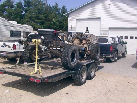 1978 Ford Bronco - A vehicle chassis and drivetrain are secured to a trailer, with a pickup truck and RV visible in the background.