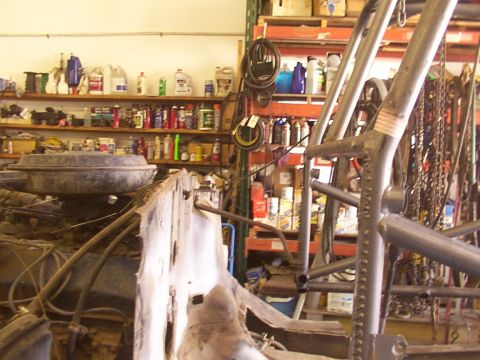 1978 Ford Bronco - A workshop scene shows the front end of a vehicle under construction, with shelves stocked with various automotive fluids and supplies.