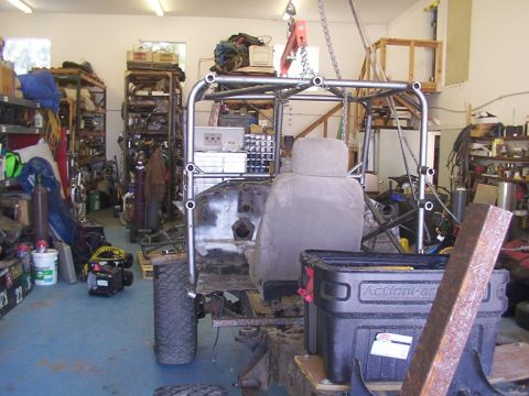 1978 Ford Bronco - A vehicle chassis is being worked on in a cluttered garage, with a roll cage and seat visible.