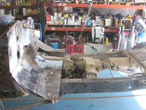 1978 Ford Bronco - The chassis of a vehicle, showing the drivetrain components, is in a state of disrepair within a cluttered garage.
