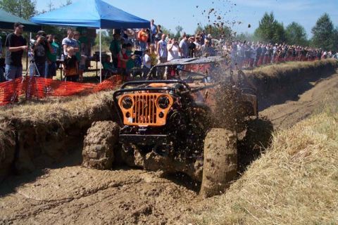 1977 Ford F-150 - A modified Jeep CJ-5 navigates a muddy track with spectators watching.