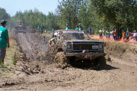 1977 Ford F-150 - A truck navigates a muddy track during a mud bogging event, with spectators watching from the sidelines.