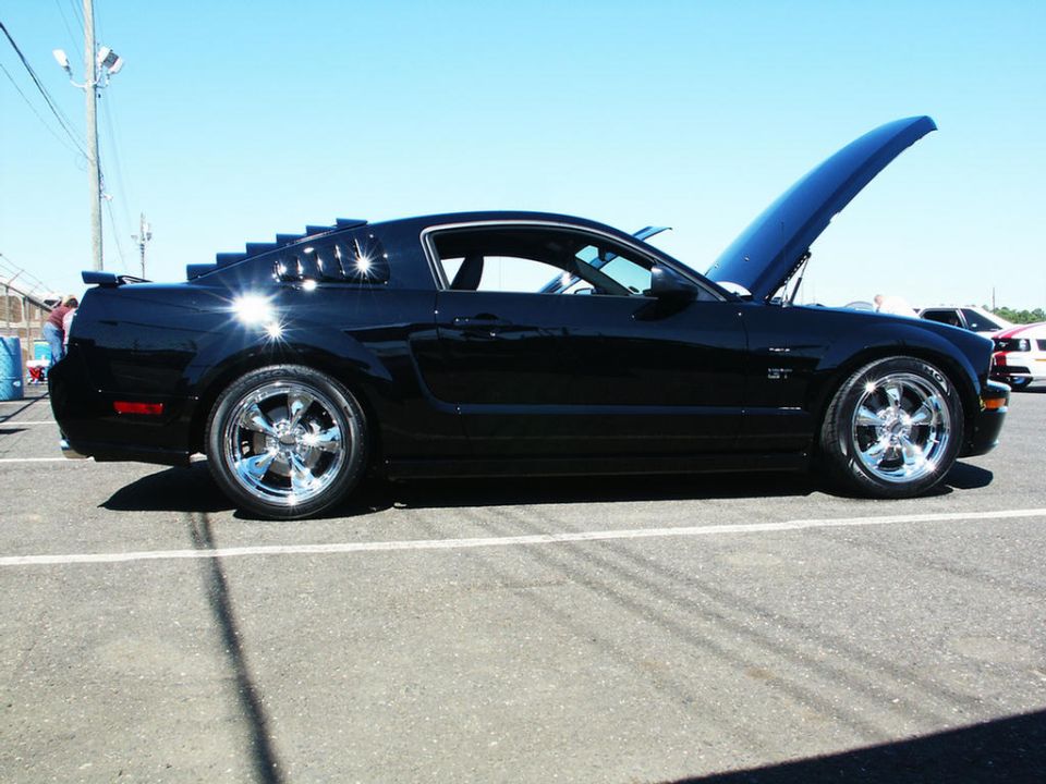 Black Ford Mustang coupe with aftermarket window louvers and chrome wheels, hood open