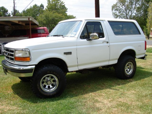White Ford Bronco SUV with lift and chrome wheels, driver-side front three-quarter view on grass