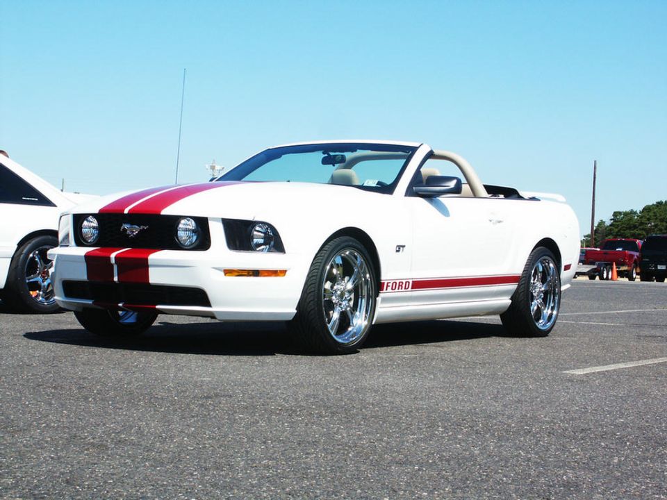 White Ford Mustang convertible with red racing stripes on hood and side. GT badge visible