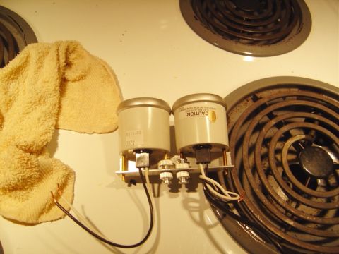 1986 Ford Bronco - Pair of round gauges still joined on a shared metal mounting bracket, sitting face-down on a white electric range top with their wiring pig…