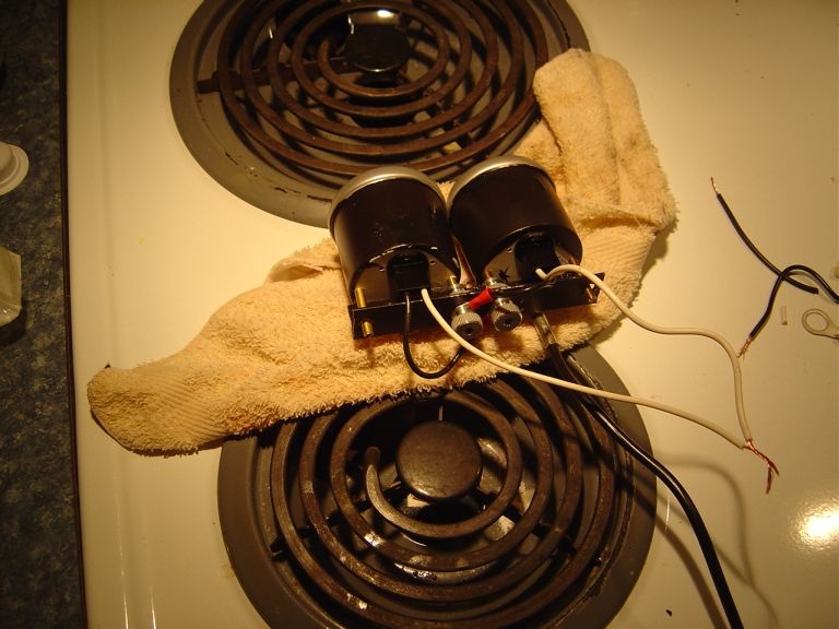 Two black-painted gauges on a bracket with wiring pigtails on a towel over a stovetop