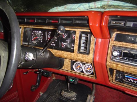 1986 Ford Bronco - Interior dashboard view of a truck/SUV with red trim and simulated woodgrain accents, showing the factory gauge cluster, column-mounted aut…