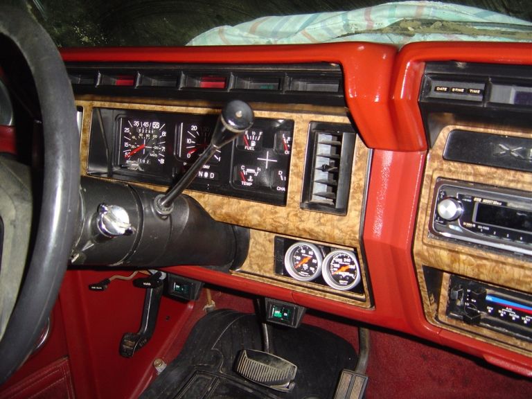Red and woodgrain dashboard with factory gauges, column shifter, aftermarket radio and dual auxiliary gauges