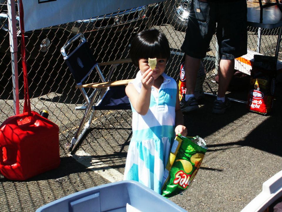Girl in a blue and white striped dress holds a chip up to her eye and a bag of chips