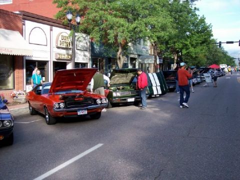 1972 Ford Ranchero - An orange muscle car with its hood open is parked on a street lined with other vehicles and buildings.