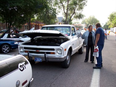 1972 Ford Ranchero - Two people discuss a white pickup truck with its hood open, parked on a street with other vehicles present.
