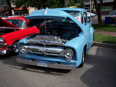 1972 Ford Ranchero - A light blue 1956 Ford F-100 pickup truck is displayed with its hood open, parked next to a red 1955 Chevrolet Bel Air.