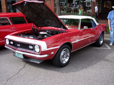 1972 Ford Ranchero - A red convertible with its hood up is parked on a street, with another red vehicle to its left.