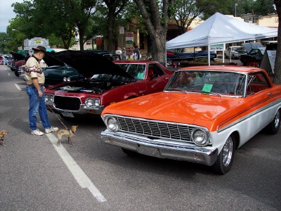 1972 Ford Ranchero - Orange and white 1964 Ford Falcon coupe at a car show. A man walks his dogs past a red car.