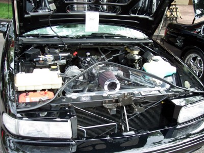 1972 Ford Ranchero - The engine bay of a black car is open, revealing the engine components and a sign with the number 310.