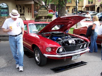 1972 Ford Ranchero - A red 1969 Ford Mustang Mach 1 is displayed with its hood open, revealing the engine, while onlookers observe.