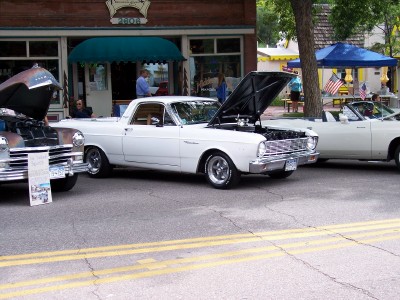 1972 Ford Ranchero - A white 1965 Ford Ranchero is displayed with its hood open, parked alongside other vehicles on a street.