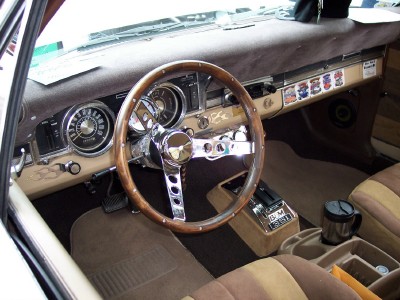 1972 Ford Ranchero - The interior of a 1972 Ford Ranchero features a wood-rimmed steering wheel and a tan dashboard with various stickers.