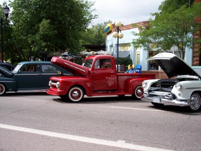 1972 Ford Ranchero - A classic red pickup truck is displayed with its hood open, alongside other vintage cars on a street.