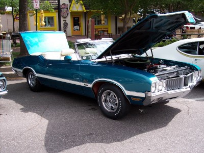 1972 Ford Ranchero - Teal convertible with white stripe and hood open, parked on street with buildings in background.
