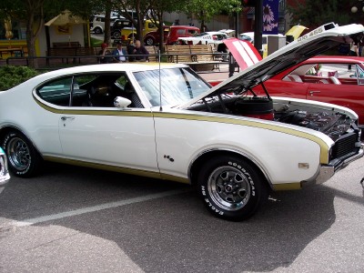 1972 Ford Ranchero - White 1970 Oldsmobile 442 with gold stripe and hood open, parked next to a red car.