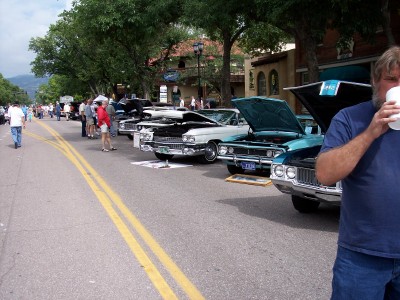 1972 Ford Ranchero - A street lined with vintage automobiles, some with engines exposed, suggests a car show or gathering.