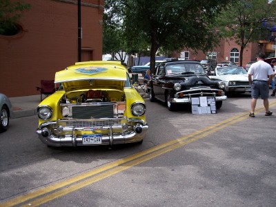 1972 Ford Ranchero - A yellow 1955 Chevrolet Bel Air is displayed with its hood open, revealing the engine, at an outdoor car show.