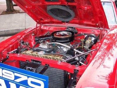1972 Ford Ranchero - The engine bay of a red 1970 vehicle is visible with the hood open, revealing the V8 engine and a blue sign.