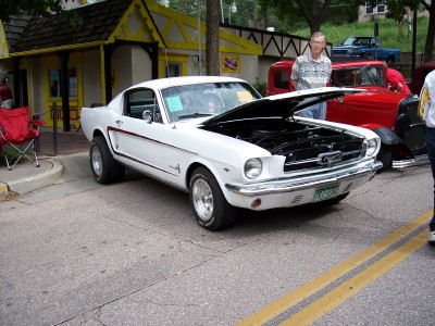 1972 Ford Ranchero - A white 1965 Ford Mustang Fastback is displayed with its hood open, parked alongside other vehicles.