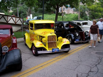 1972 Ford Ranchero - A row of vintage vehicles, including a bright yellow hot rod truck, are parked on a street.