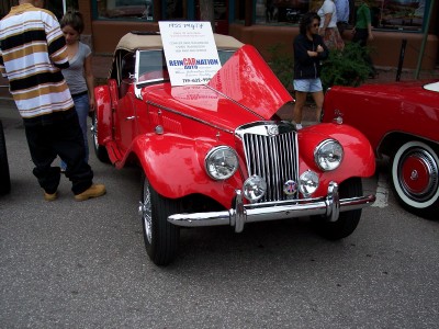 1972 Ford Ranchero - 1955 MG TF convertible on display, hood open, with a sign detailing its information.