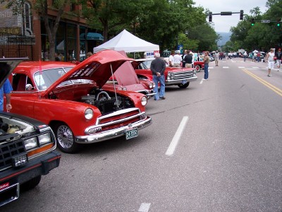 1972 Ford Ranchero - A street fair or car show features several vintage vehicles with their engines exposed for viewing.