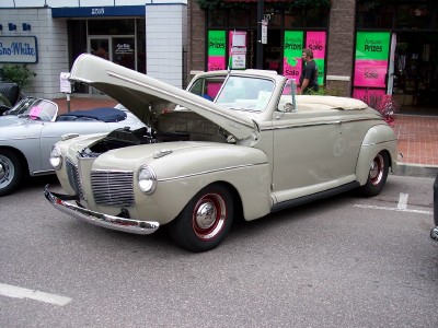 1972 Ford Ranchero - A tan convertible from the 1940s is parked on a street with its hood up, next to another car.