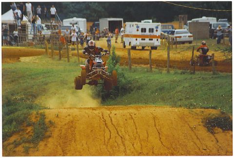 1992 Ford Mustang - A motocross event is underway with an ATV rider catching air on a dirt track.