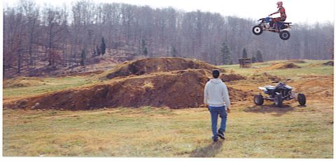 1992 Ford Mustang - An ATV rider soars through the air above a dirt track, while another ATV waits on the ground.