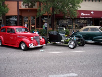 1972 Ford Ranchero - Three vintage automobiles are displayed on a street in front of storefronts.