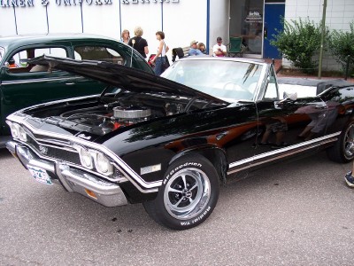 1972 Ford Ranchero - A black convertible with its hood open, revealing the engine. It features chrome trim and distinctive racing wheels.