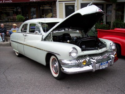 1972 Ford Ranchero - 1951 Mercury Eight sedan, hood up, parked on a street with buildings in the background.