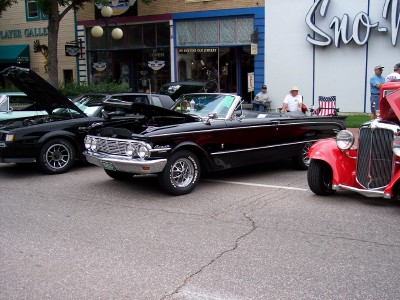 1972 Ford Ranchero - A black convertible with its hood up is parked on a street next to other vehicles.