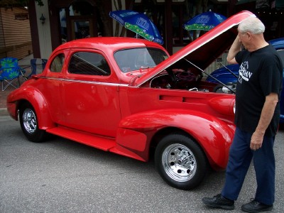 1972 Ford Ranchero - A man inspects the engine of a bright red classic coupe with its hood raised.