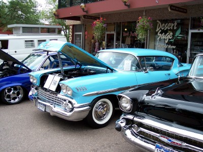 1972 Ford Ranchero - A row of classic cars, including a bright blue 1958 model with its hood raised, are parked outside a storefront.