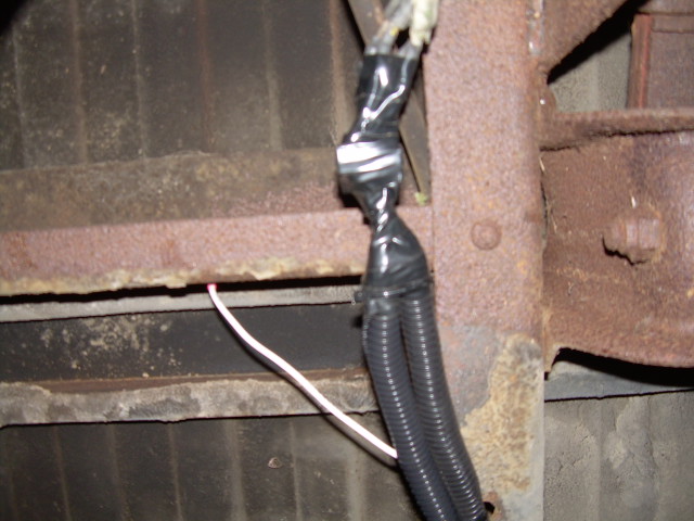 Taped split-loom wiring harness branch running down a rusty truck frame rail