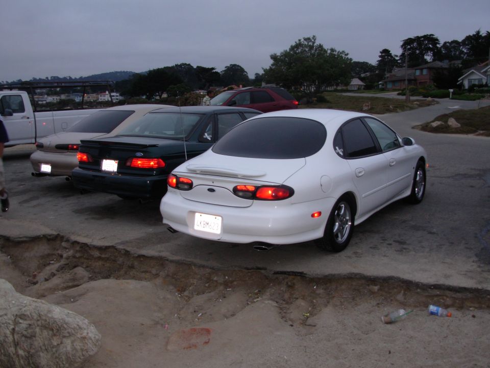 White Ford Taurus parked next to a dark green Ford Taurus and a light-colored pickup truck