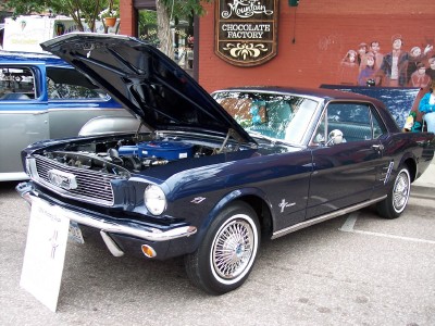 1972 Ford Ranchero - A dark blue 1965 Ford Mustang is displayed with its hood open, parked on a street in front of a building with a "Chocolate Factory" sign.
