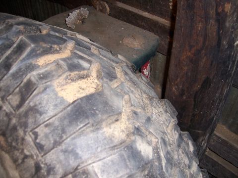1983 Ford Bronco - A close-up view of a tire and wooden structural elements, likely in a storage area.