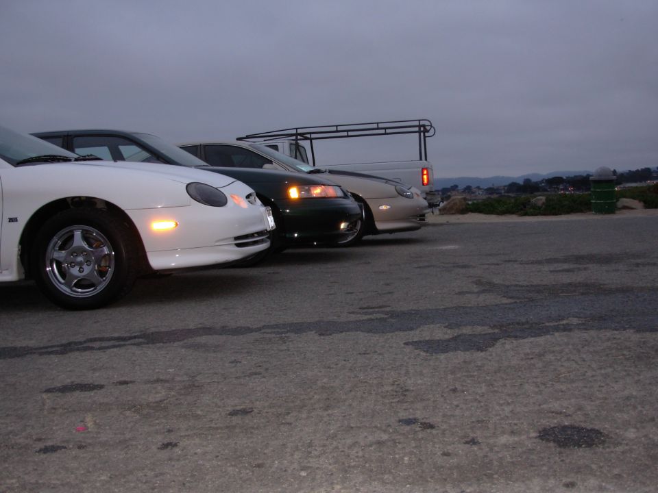 White 1995 Ford Taurus in front, dark sedan in middle, beige sedan behind. Truck rack visible