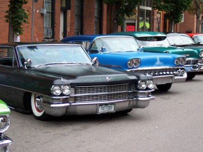 1972 Ford Ranchero - A row of classic cars, including a black Cadillac and a blue Chevrolet, are parked along a street.