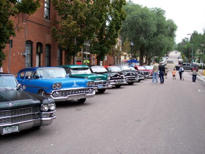 1972 Ford Ranchero - A row of vintage automobiles are parked along a brick building on a cloudy day.